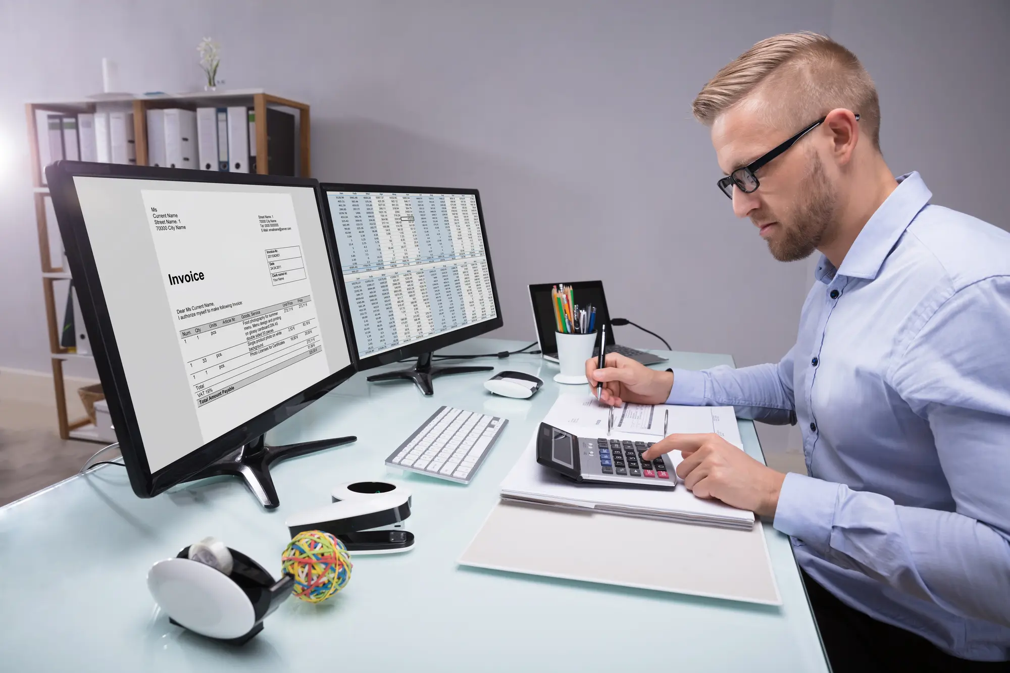 Man working in office with two desktops and calculating finances, representing Xero accounting services in New Zealand